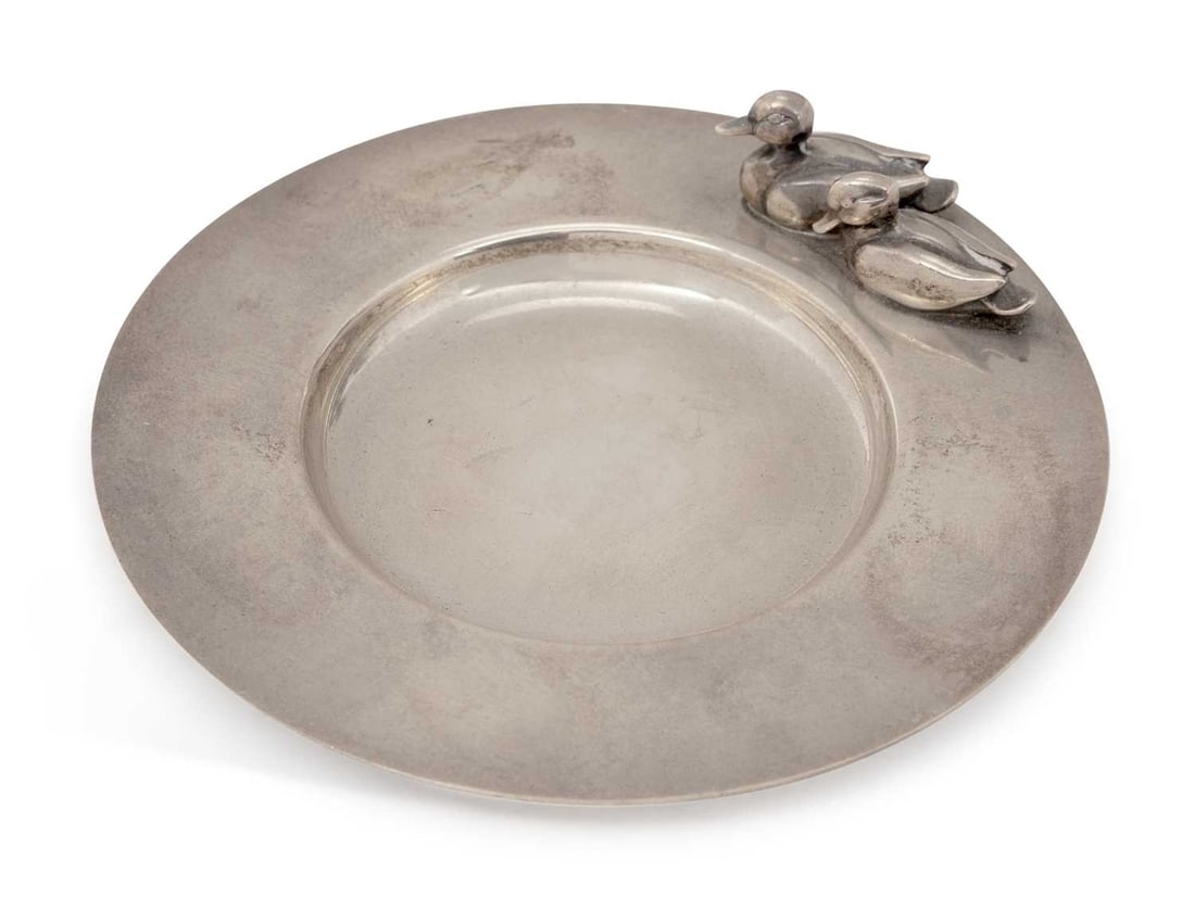 SARAH JONES: AN ELIZABETH II SILVER PIN DISH: London 1990, of plain circular form, with a pair of cast ducks to rim. 10cm diameter, 2.7 troy ounces Good condition overall, with light surface scratches throughout and a small dent to rim.