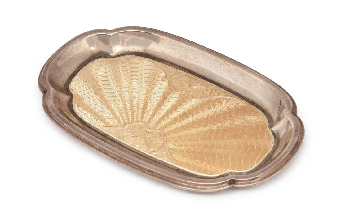 A GEORGE V SILVER AND ENAMEL PIN TRAY / TRINKET DISH: by Barker Brothers Silver Ltd., Birmingham 1932, of shaped rectangular form, decorated with cream coloured enamel with sunburst foliate pattern. 12.5cm wide, 1.7 troy ounces Good condition overall,