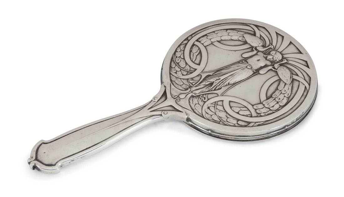 AN ART NOUVEAU SILVER HAND MIRROR: by William Hutton & Sons Ltd, London 1906, of circular form with a shaped handle, the back is decorated with a semi-nude woman holding a peacock in either hand. 28cm long, 14.2 troy ounces gross