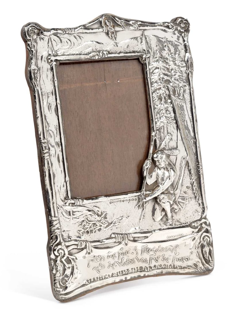 AN EDWARDIAN SILVER-MOUNTED PHOTOGRAPH FRAME: by J B & Co, Birmingham 1904, the mount repousse decorated with a scene from Hiawatha, a figure paddling a canoe before pine trees, the canoe stamped HIAWATHA, the base with a banner inscribed FEED TH