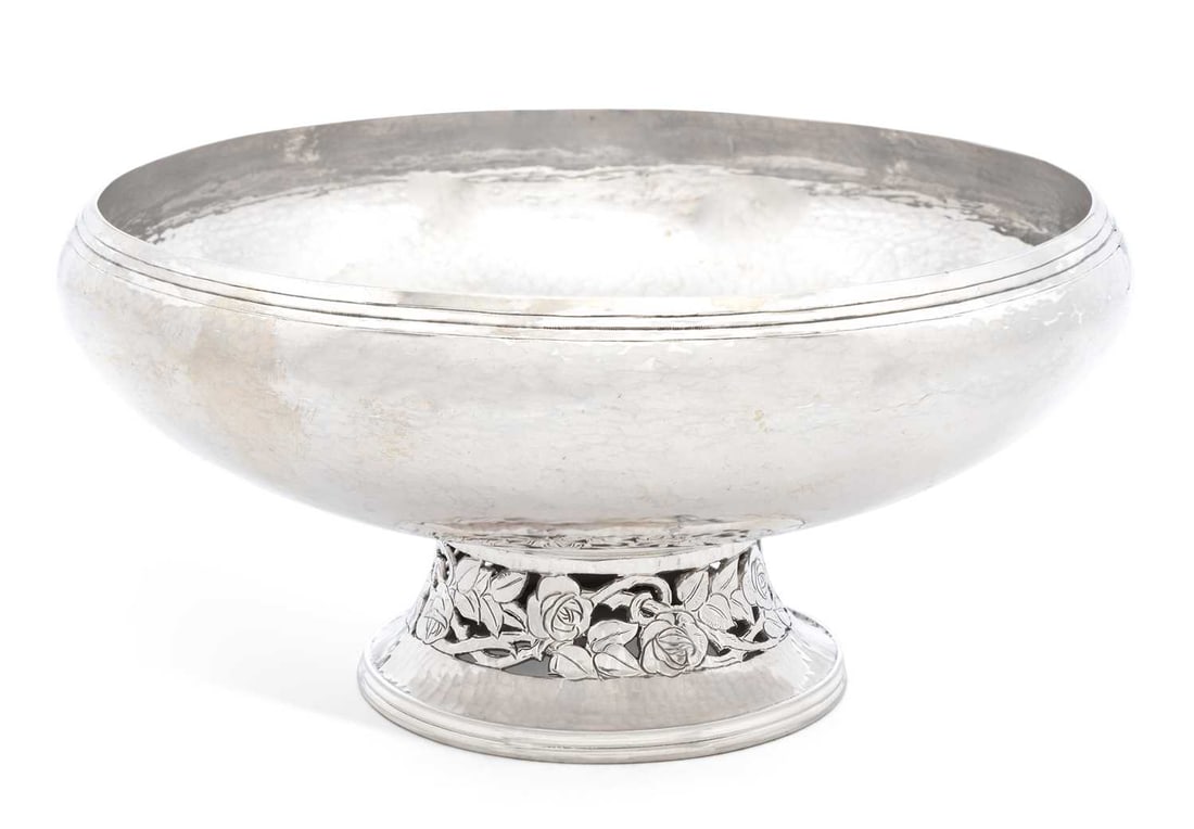 A GEORGE VI SILVER ARTS AND CRAFTS PEDESTAL BOWL: by Hugh Wallis, Chester 1937, of squat circular form, planished with reeded rim, on a spreading circular foot decorated with a pierced foliate rose band. 22.5cm diameter, 20.4 troy ounces Good