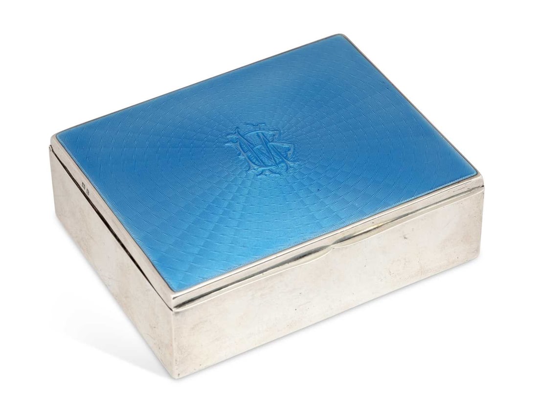 A GEORGE V SILVER AND ENAMEL CIGARETTE BOX: by Adie Brothers, Birmingham 1929, of rectangular form, the hinged cover decorated with blue enamel, monogrammed to centre, plain sides and cedar lined. 11.3cm wide Good condition overall, light