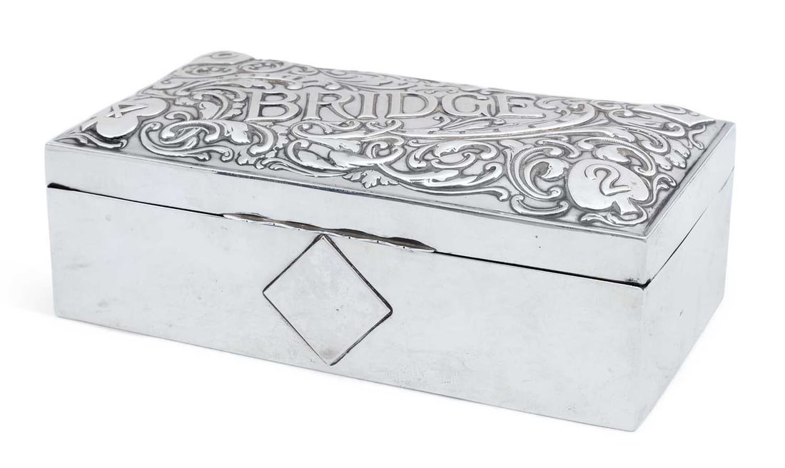 AN EDWARDIAN SILVER BRIDGE BOX: by Levi & Salaman, Birmingham 1905, of rectangular form, the hinged cover repousse decorated with Bridge, scroll motif and card suits to corners, fitted leather-lined interior and covered base. 20cm