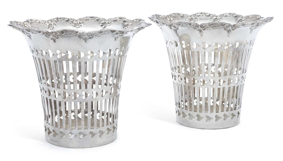 A PAIR OF EDWARDIAN SILVER PLANTERS: by Walker & Hall, Sheffield 1907, of cylindrical form with a scalloped rim embossed with floral motifs, the body pierced with vertical geometric slits and horizontal heart shapes. (2) 13cm high, 13.5