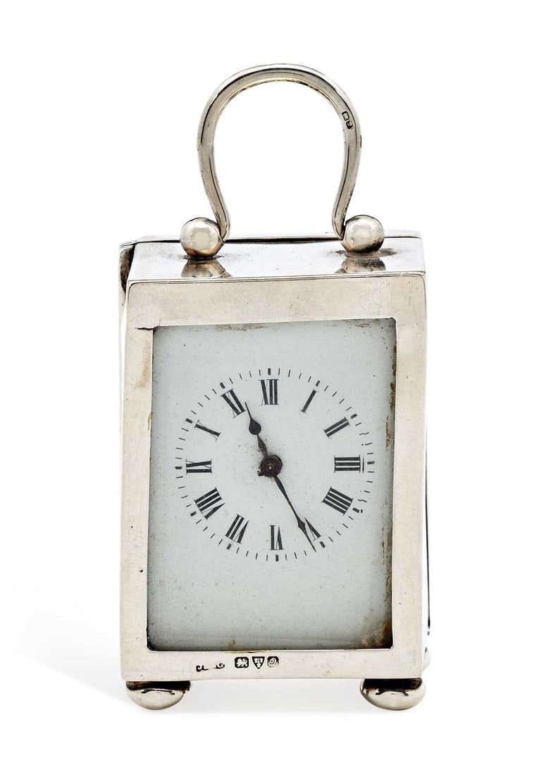 A GEORGE V SILVER-CASED TRAVELLING CLOCK: by J & R Griffin, Chester 1916, the rectangular case with a hinged swing handle, on bun feet, the white enamel dial with Roman numerals, French movement. 6.5cm high (excl. handle) Winds but not curren