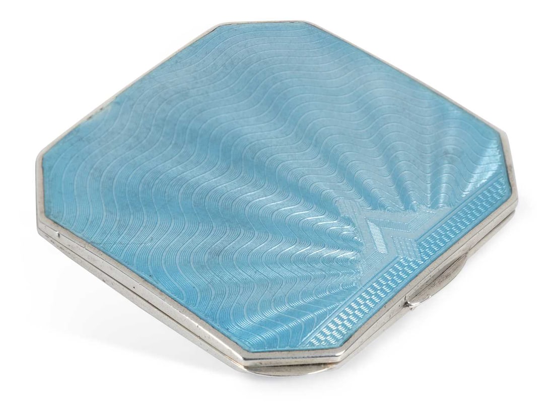 AN ART DECO SILVER AND ENAMEL COMPACT: by William Neale, Birmingham 1934, retailer's stamp J.C. Vickers, 145 Regent Street, W., of square form with canted corners, the hinged cover with powder blue enamel in a radiating pattern, inset with