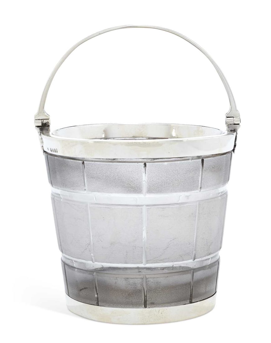 A VICTORIAN SILVER-MOUNTED CUT-GLASS ICE PAIL: maker's mark IE, London 1864, of barrel form with a swing handle engraved with lion and dog crests, leaf shaped mounts, the textured glass frosted. 9cm high, 10.5cm diameter Good condition overall -
