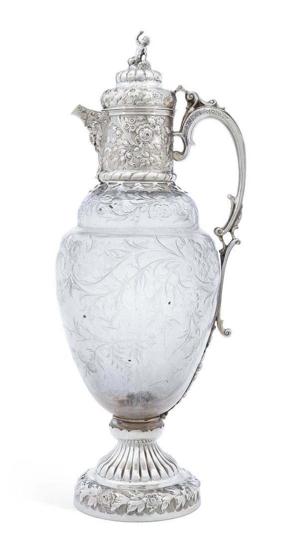 A LATE VICTORIAN SILVER-MOUNTED AND 'ROCK CRYSTAL' STYLE CLARET JUG: by Charles Edwards, London 1891, of baluster form, the domed hinged cover with figural bacchanalian putti finial, the mounts chased with floral decoration, the glass body engraved with flora and