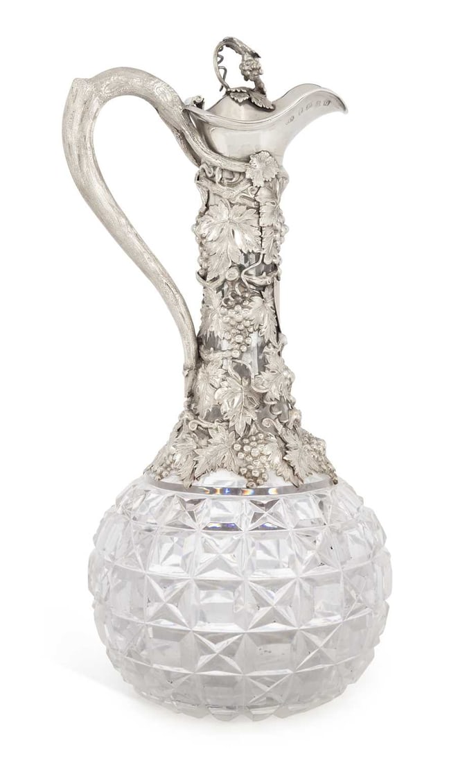 A VICTORIAN SILVER-MOUNTED CUT-GLASS CLARET JUG: by Cronin and Wheeler, Birmingham 1865, with an elaborately cast mount of fruiting vine issuing from a branch handle, the hinged cover with a grape finial. 30cm high