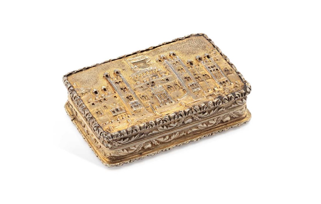 AN EARLY VICTORIAN 'CASTLE TOP' SILVER-GILT VINAIGRETTE: by Nathaniel Mills, Birmingham 1838, of rectangular form with hinged cover, decorated in relief with a view of Windsor Castle within foliate borders, opening to a pierced grille, vacant cartouche to