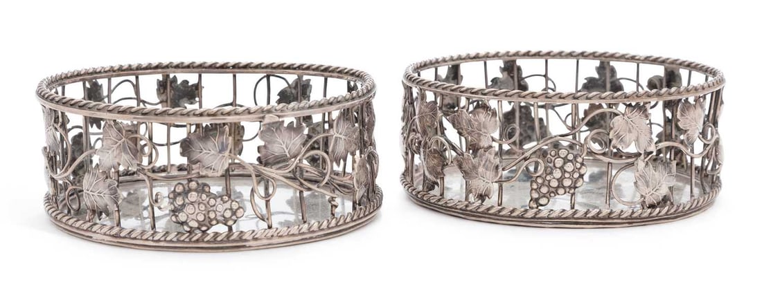 A PAIR OF GEORGE III SILVER COASTERS: unmarked, manner of William Plummer, of circular form, open wire colonnade with applied chased fruiting vines, with twist borders, engraved with dog crest, weighted. (2) 11cm wide Both with misshapen