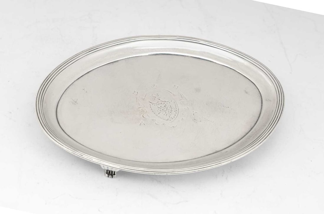 A GEORGE III SILVER TEAPOT STAND: by Peter & William Bateman, London 1806, of oval form with reeded border, armorial engraved, on four tapering feet. 17.2cm wide, 5.1 troy ounces Good condition overall in commensurate with age. Not si