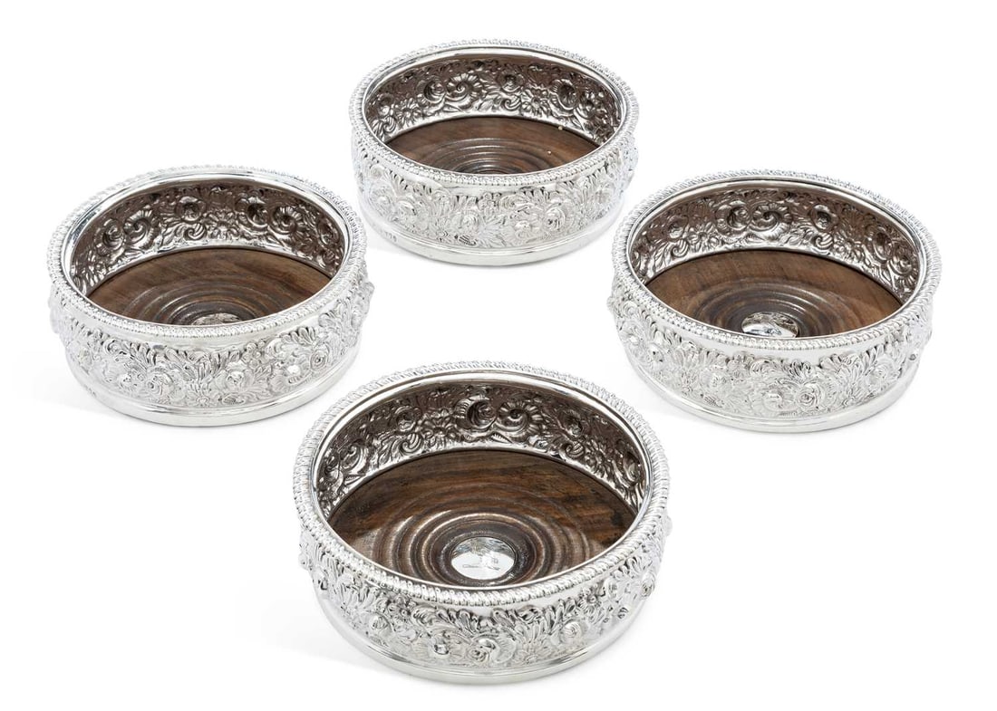 A SET OF FOUR GEORGE III SILVER WINE COASTERS: by John & Thomas Settle, Sheffield 1817, each of circular form with gadrooned rim, the sides embossed and chased with roses, flowers and foliate scrolls, the turned wood base inset with a silver boss 