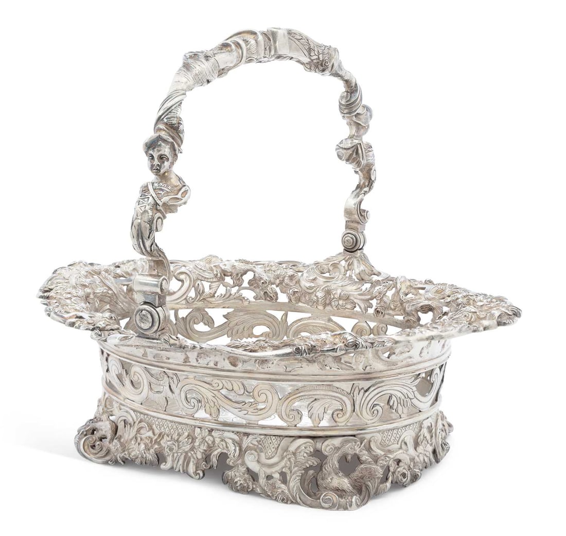 A LARGE GEORGE III SILVER PIERCED CAKE BASKET: maker's mark I.C., London 1808, of oval form, Rococo revival style, the swing handle cast in high relief with figural shoulders, foliate cornucopia and scrolls, the rim cast with mythical beasts among