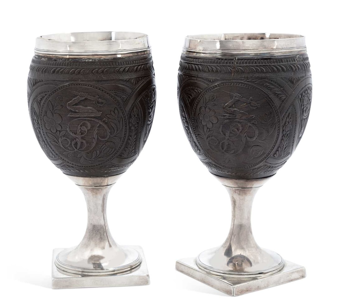 A PAIR OF GEORGE III SILVER-MOUNTED COCONUT CUPS: makers marks T.H., London 1799, each with carved coconut bowl decorated with floral bouquets and tulip motif surrounded by shaped borders, an oval carved with monogram SP beneath an armorial featuring