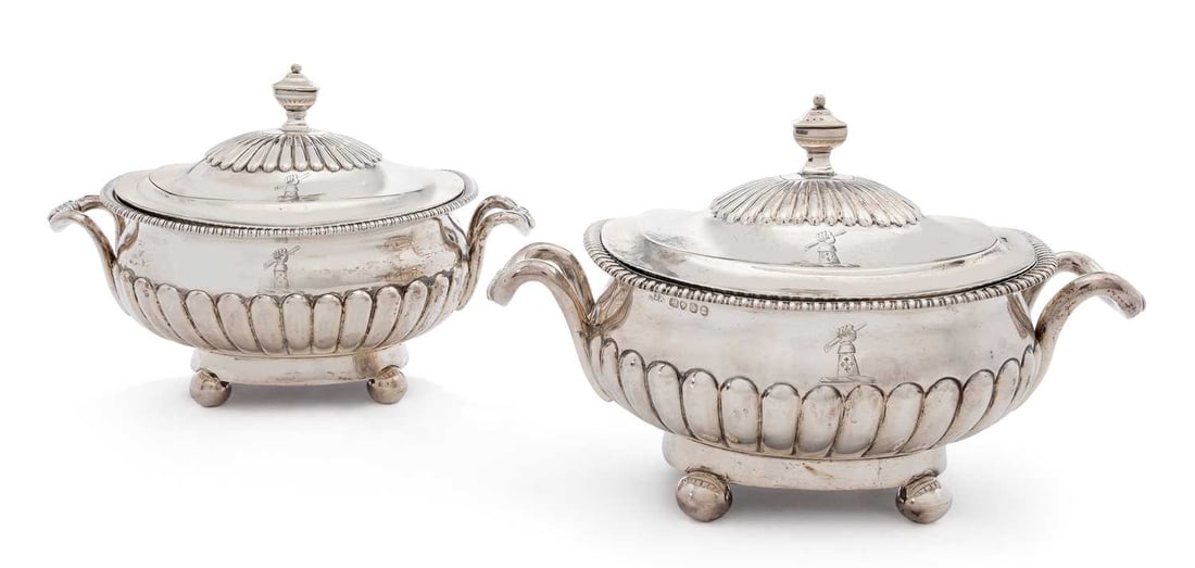 A MATCHED PAIR OF GEORGE III / GEORGE IV SILVER COVERED TUREENS: by Robert Hennel I & Samuel Hennel, London 1807, and by Joseph Angell I, London 1824, each of rectangular form with curved angles, demi-lobed body and cover, with urn finial, the covers engraved with 