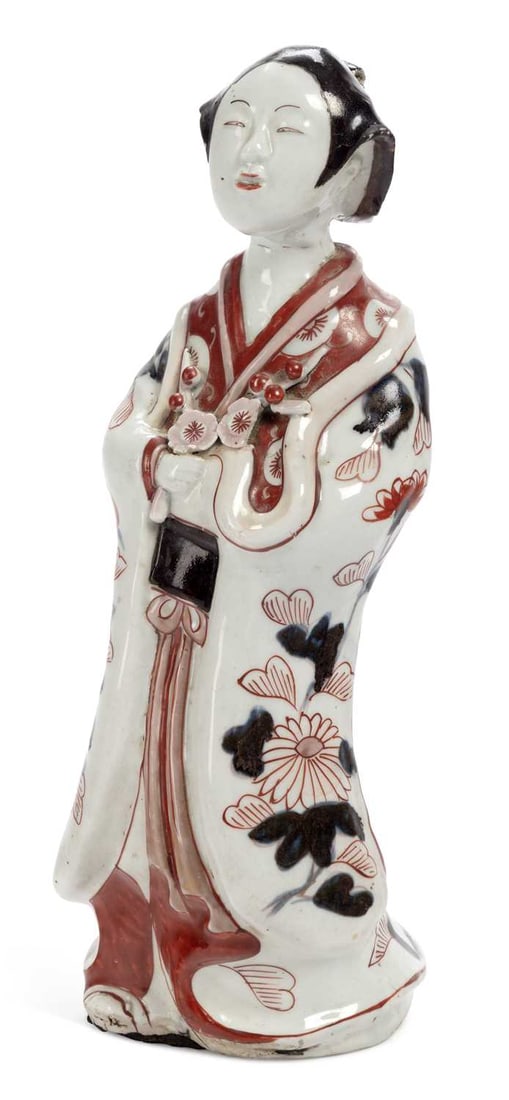 A JAPANESE ARITA FIGURE OF A BIJIN LATE 17TH CENTURY: modelled standing with the hands clasped before her, wearing a kimono decorated in underglaze blue, iron-red and black with peonies, chrysanthemums and scattered blossom, the sash tied at the front, t