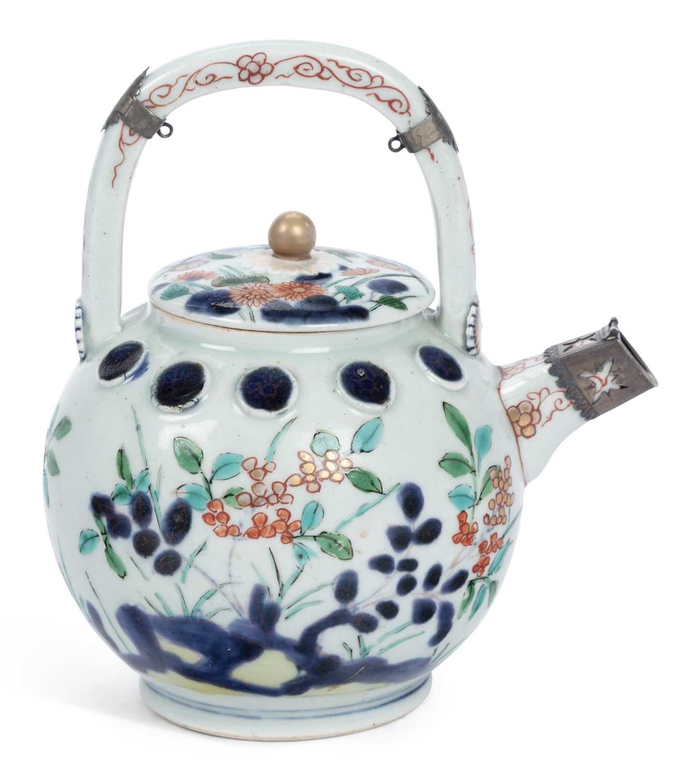 A JAPANESE ARITA PORCELAIN TEAPOT AND COVER LATE 17TH/ EARLY 18TH CENTURY: of globular form with an overhead loop handle, the shoulder applied with a band of circular bosses in underglaze blue, the body painted in underglaze blue and enamels with flowering plants issuing fro