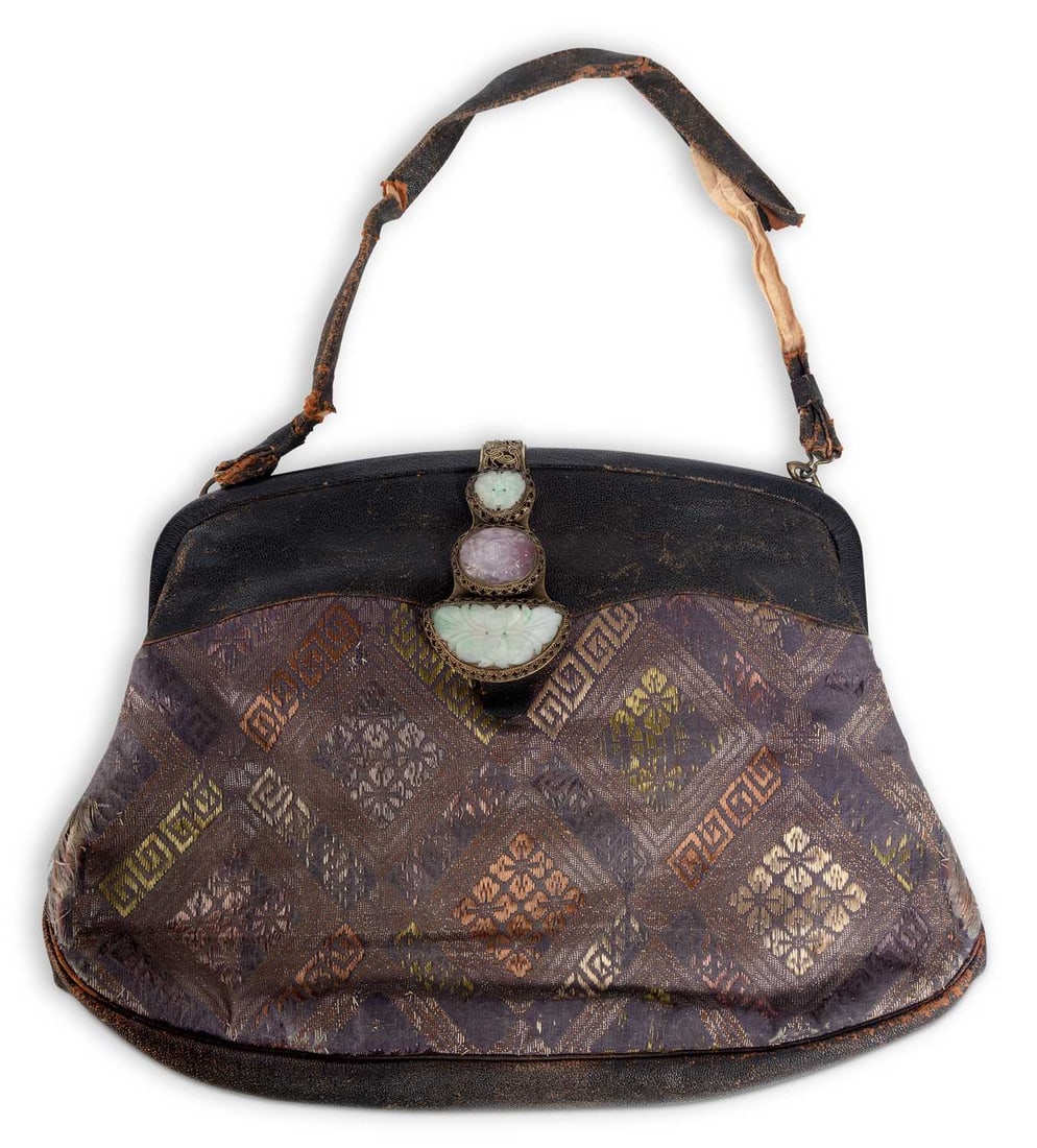A JADE MOUNTED BROCADE AND LEATHER HANDBAG EARLY 20TH CENTURY: the black leather body inset with a panel of Chinese silk brocade woven with key fret and floral roundels within a lozenge diaper, the gilt-metal filigree clasp set with three carved jade panels, the 