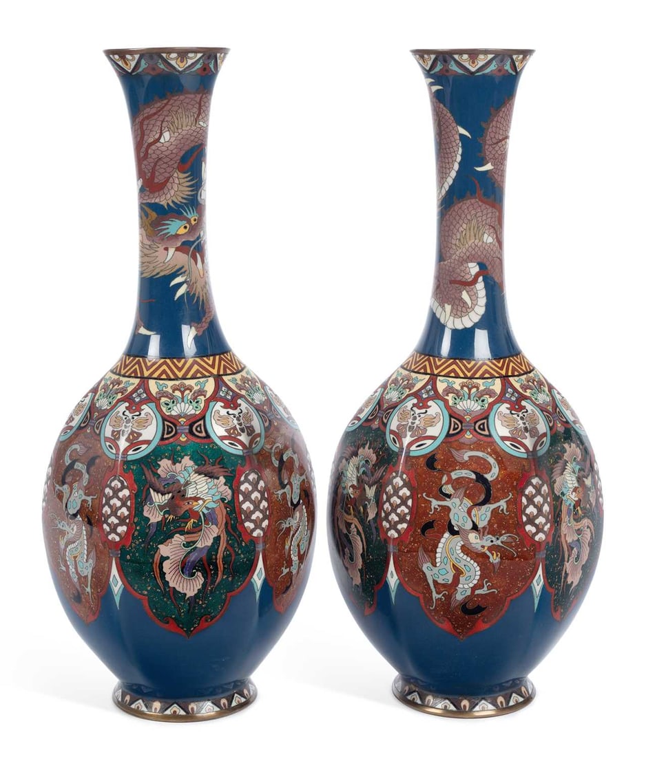 A PAIR OF JAPANESE CLOISONNE ENAMEL VASES MEIJI PERIOD: of bottle form with tall flared necks, the necks worked in coloured enamels and wire with a dragon coiling on a midnight blue ground, the bodies with phoenix and dragons within shaped lappet panels, b