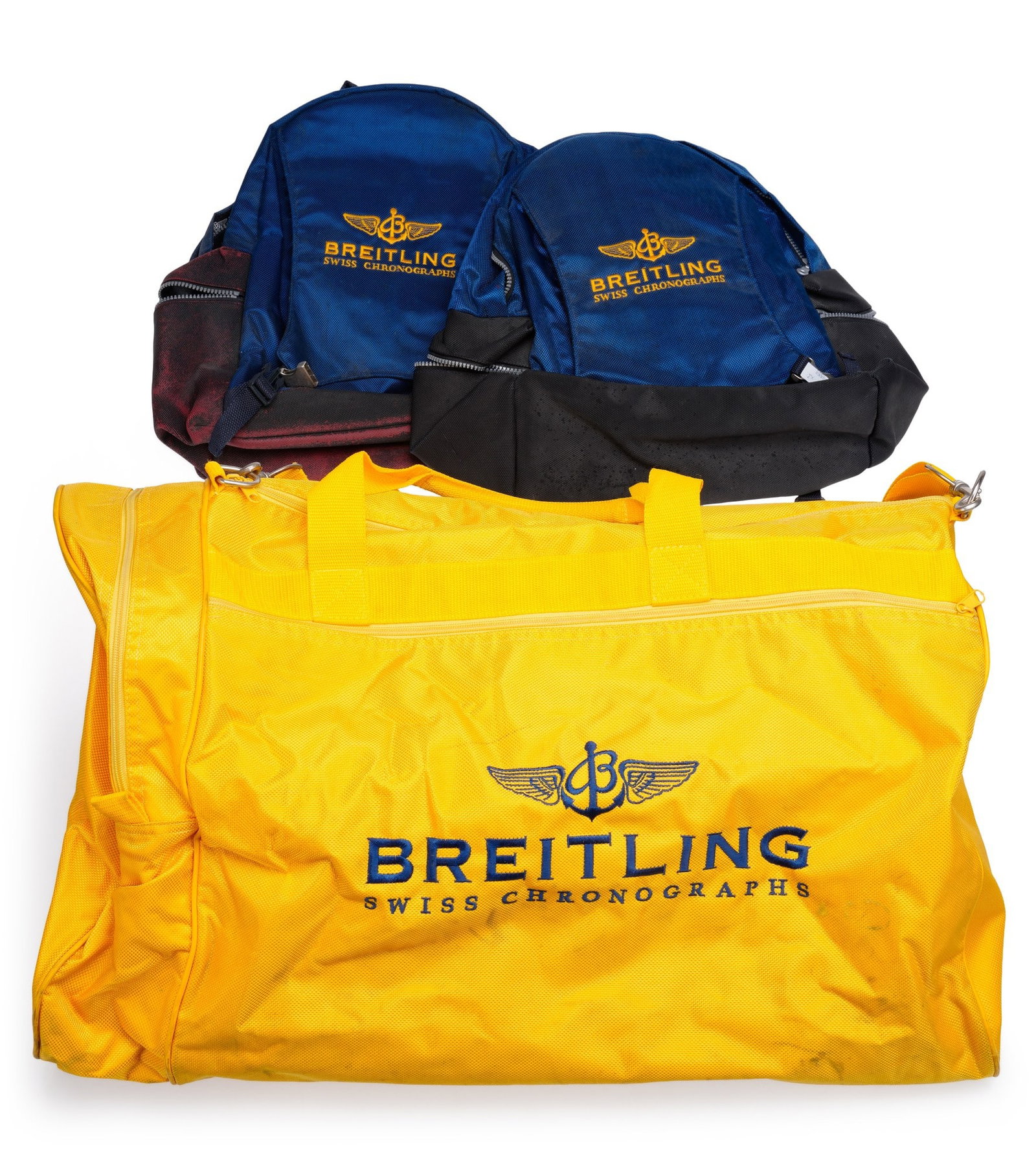 A BREITLING HOLDALL AND TWO RUCKSACKS: comprising a yellow fabric holdall with a Breitling logo on one side and a helicopter on the other; accompanied by two rucksacks in blue material both embroidered Breitling Swiss Chronographs. (3)