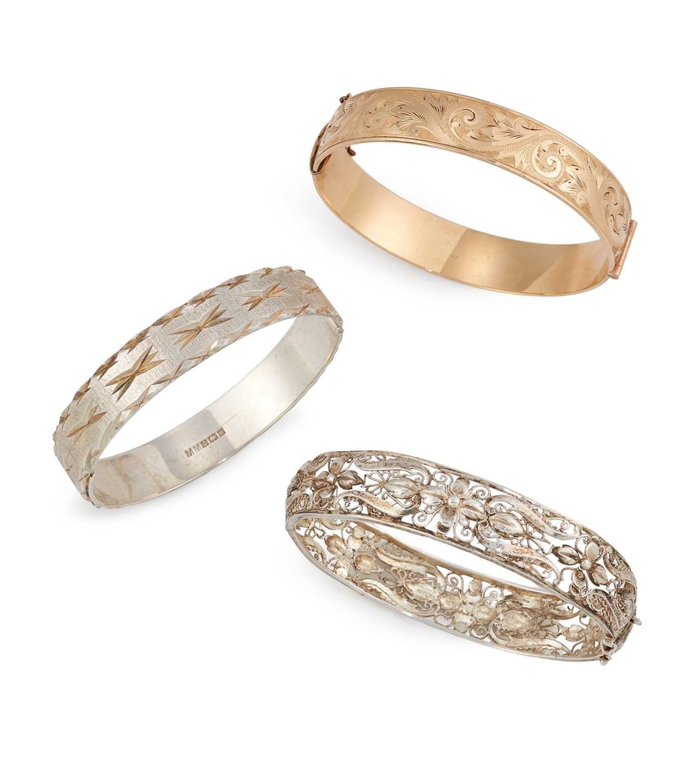 THREE HINGE OPENING BANGLES: comprising a metal core foliate engraved bangle; a filigree bangle; and a hallmarked silver bight-cut engraved bangle. (3) 17cm inner diameter and smaller, 85.5 grams gross Filigree bangle slightly