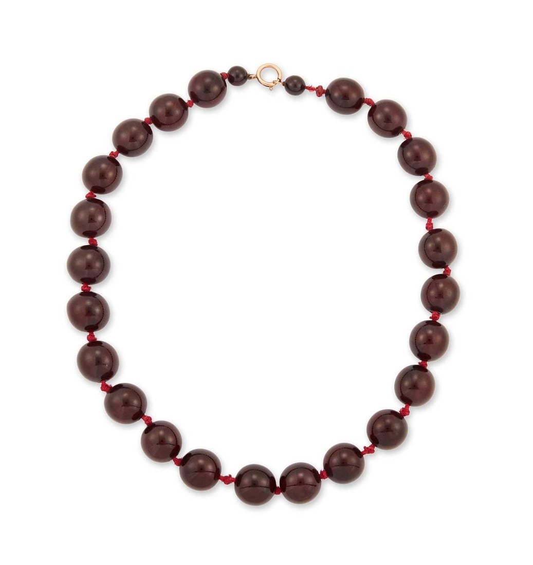A CHERRY AMBER BAKELITE BEAD NECKLACE: formed of twenty-five individually knotted uniform round beads, to a rolled gold clasp. 53.5cm long, 82 grams With internal streaking. Beads 17mm diameter approx with two small beads. Internal streaki