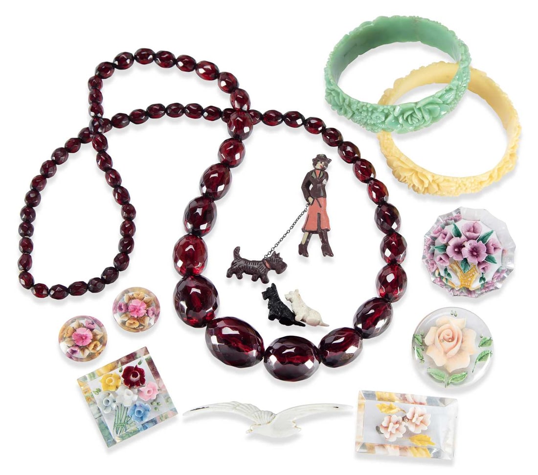 A PRYSTAL CHERRY AMBER BAKELITE BEAD NECKLACE AND A COLLECTION OF EARLY PLASTIC JEWELLERY: the necklace formed of sixty-five graduated faceted oval beads; together with two floral bangles, reverse carved lucite floral brooches, and animal brooches. (11) Necklace 80cm long