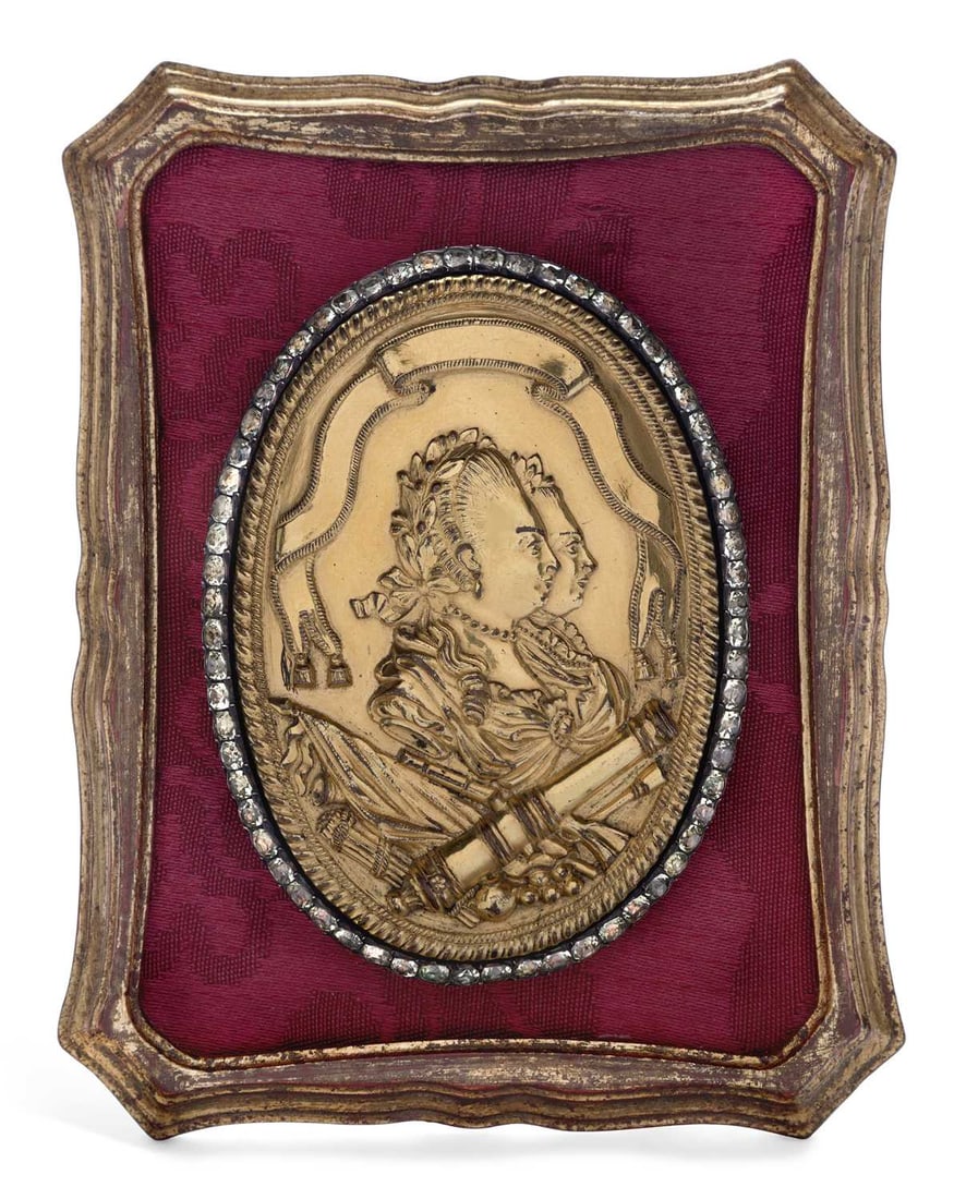 A FRENCH GILT METAL AND PASTE-SET BUCKLE 19TH CENTURY: oval form, cast with portraits of King Louis XVI and Marie Antoinette above symbols of war, within a paste border, set upon a gilt framed velvet border. 13.5cm high
