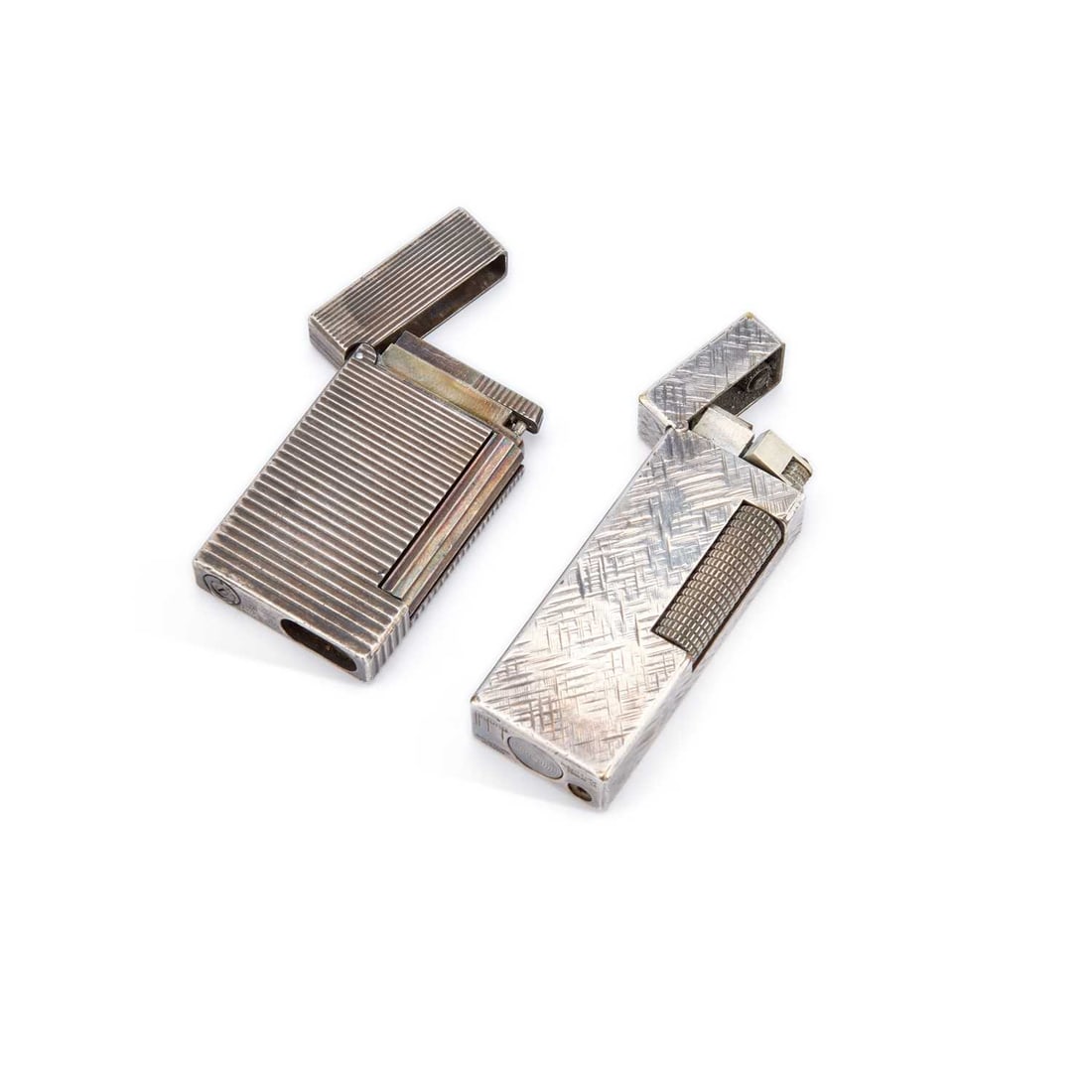 TWO SILVER PLATED LIGHTERS: comprising a St Dupont example, with reeded sides, serial no. 85ISU92, (a/f); and a Dunhill Rollagas with crosshatched sides. (2) First 5.4cm high