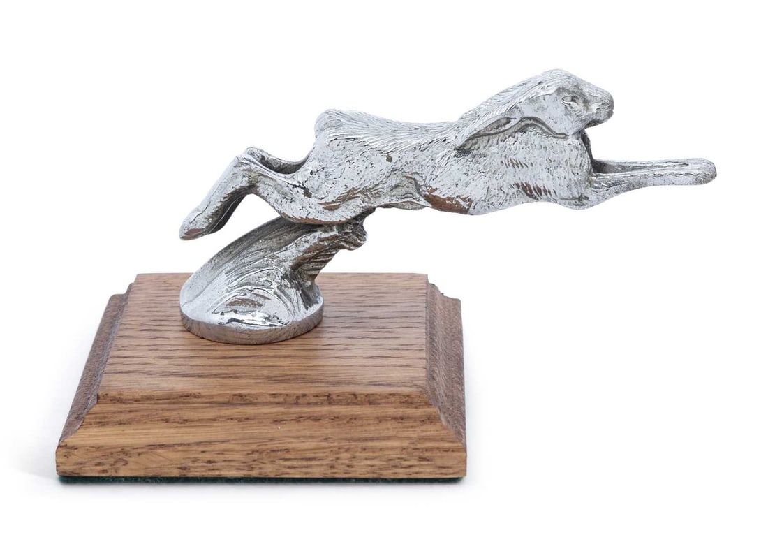 AUTOMOBILIA: A SILVER PLATED HARE CAR MASCOT 20TH CENTURY: the mascot cast as a running hare, mounted on a square oak pedestal plinth. 14.5cm long