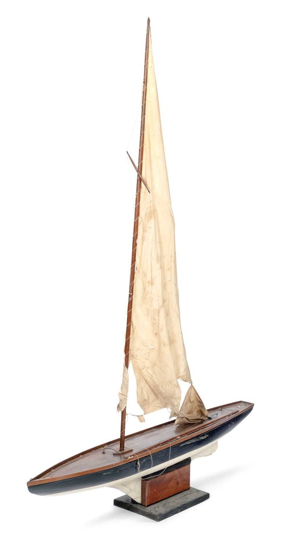 A LARGE POND YACHT 20TH CENTURY: the varnished hull with black painted topsides and white painted underbody, the deck with a single mast, boom and canvas sails with standing rigging, raised on a wooden stand with rectangular base.