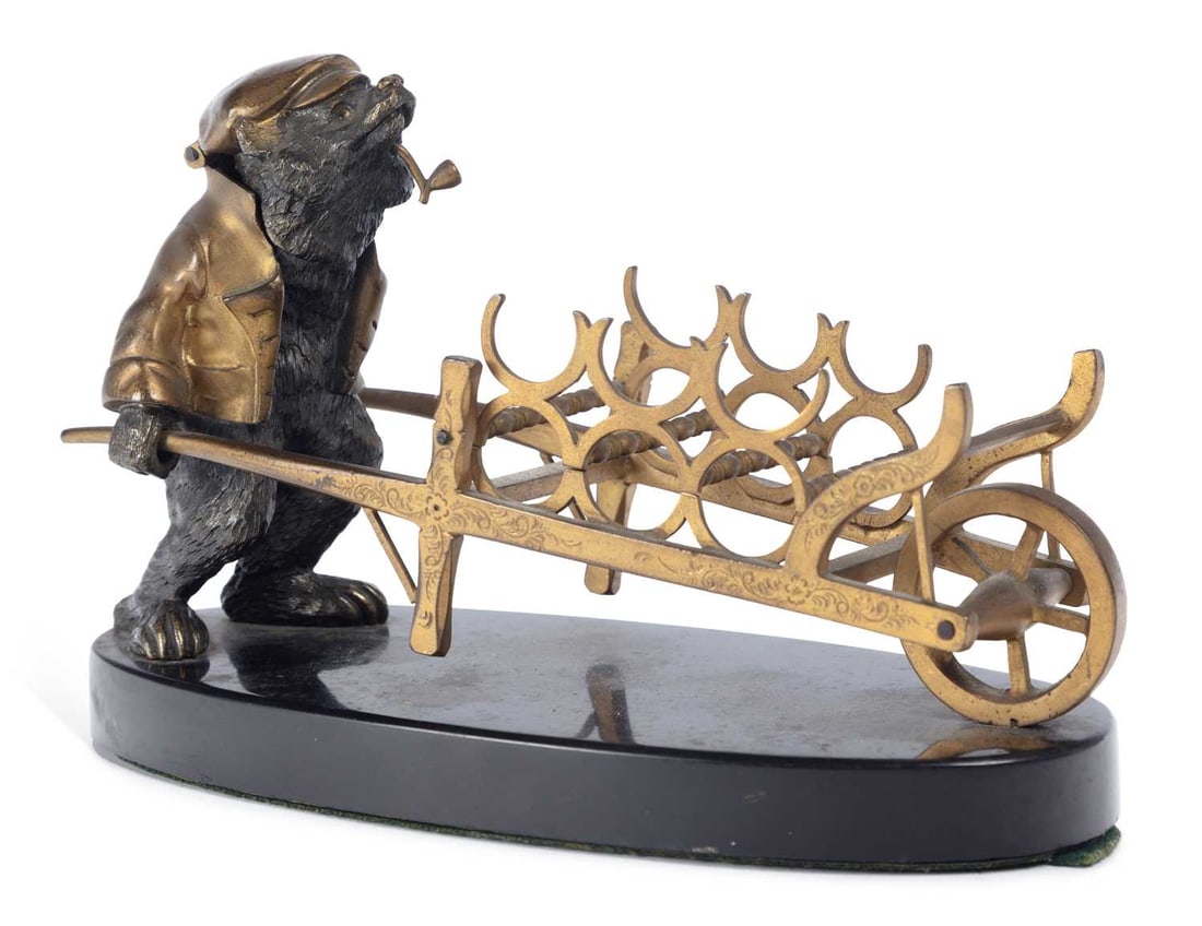 A RUSSIAN BRONZE AND GILT-METAL CIGAR HOLDER CIRCA 1880: amusingly modelled as a bronze bear, with a hinged head and wearing a jacket and flat cap, pushing a gilt-metal wheelbarrow, made to hold six cigars, set upon an oval marble base. 11.5cm high (includi