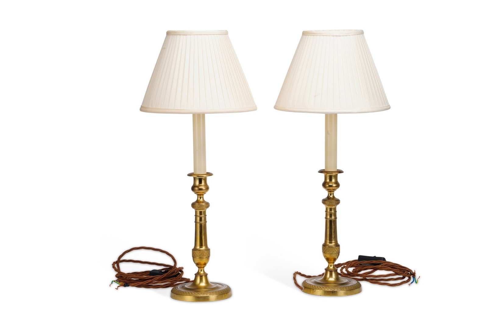 A PAIR OF FRENCH ORMOLU CANDLESTICK LAMPS: in the Empire taste, of circular form with geometric bands, with pleated ivory coloured shades. (2) 58cm high (including shades).