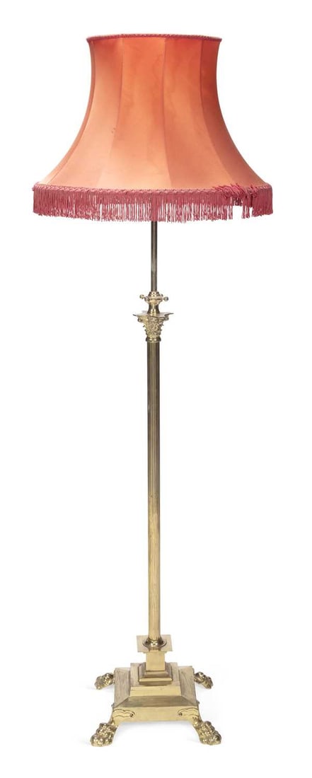AN EARLY 20TH CENTURY BRASS STANDARD LAMP: the telescopic reeded column with Corinthian capital, raised on a stepped square base with lion paw feet, with a coral fringed shade. 174cm high overall