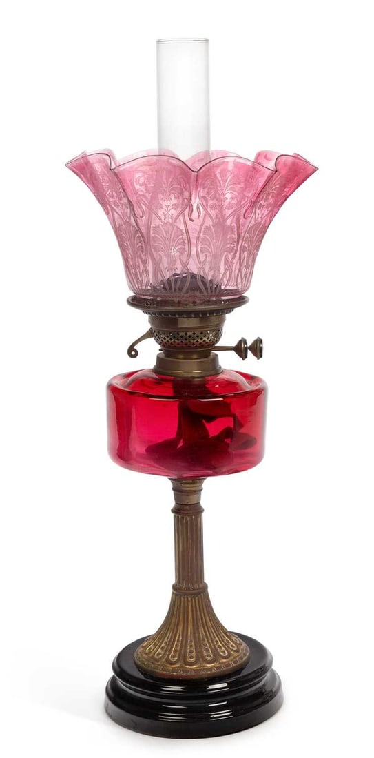 A VICTORIAN CRANBERRY GLASS AND BRASS OIL LAMP: with a foliate decorated tinted shade. 64cm high overall Glass funnel, shade and tank all in good condition, the brass with surface dirt commensurate with age,