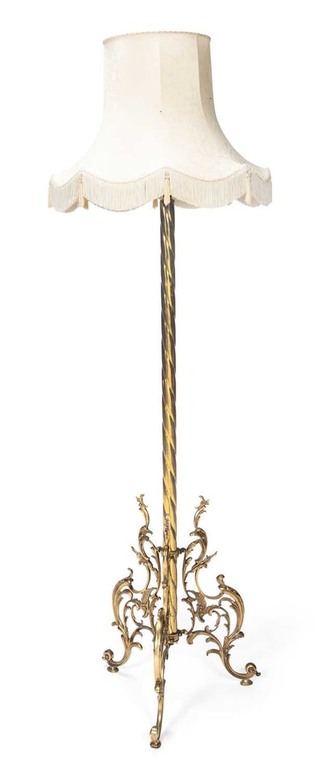 A LATE VICTORIAN BRASS STANDARD LAMP: the spirally reeded column raised on three cast foliate scroll supports with scroll feet, with a cream damask shade with fringed and tasselled border. 189cm high overall