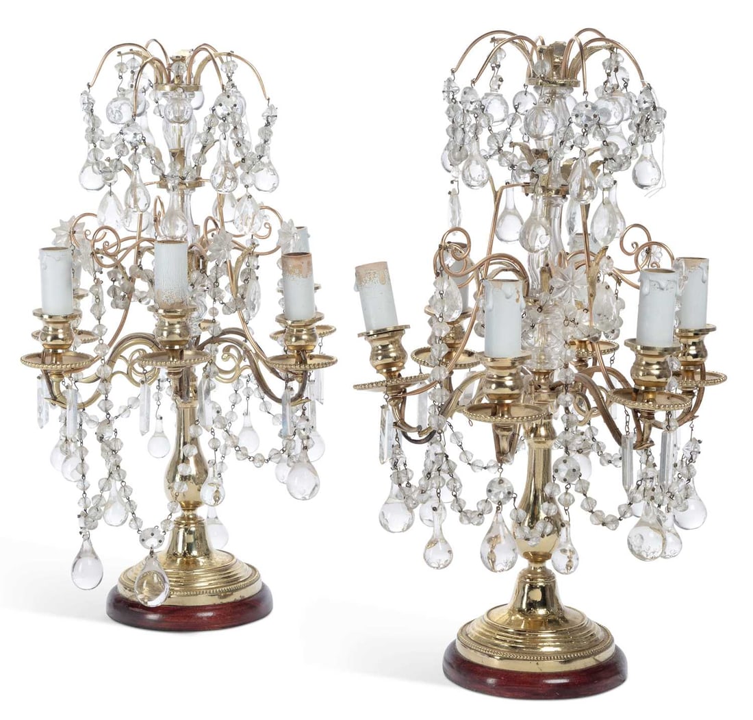 A PAIR OF GILT METAL AND CUT-GLASS FIVE-LIGHT CANDELABRA TABLE LAMPS: each with a faceted glass baluster stem issuing five scrolling branches with beaded drip pans and candle form nozzles, hung throughout with faceted lustre drops, pear drops and beaded swags beneath a