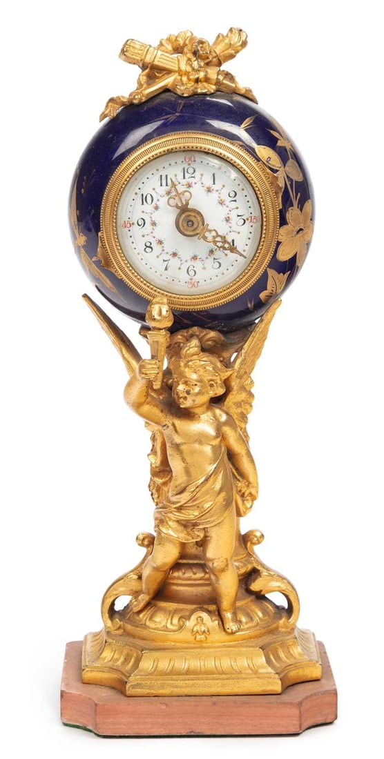 A FRENCH GILT-BRONZE AND ENAMEL CLOCK CIRCA 1870: the circular clock supported by a putti brandishing a torch, before a garland festooned classical column, set upon a rosso antico marble base. 21.5cm high
