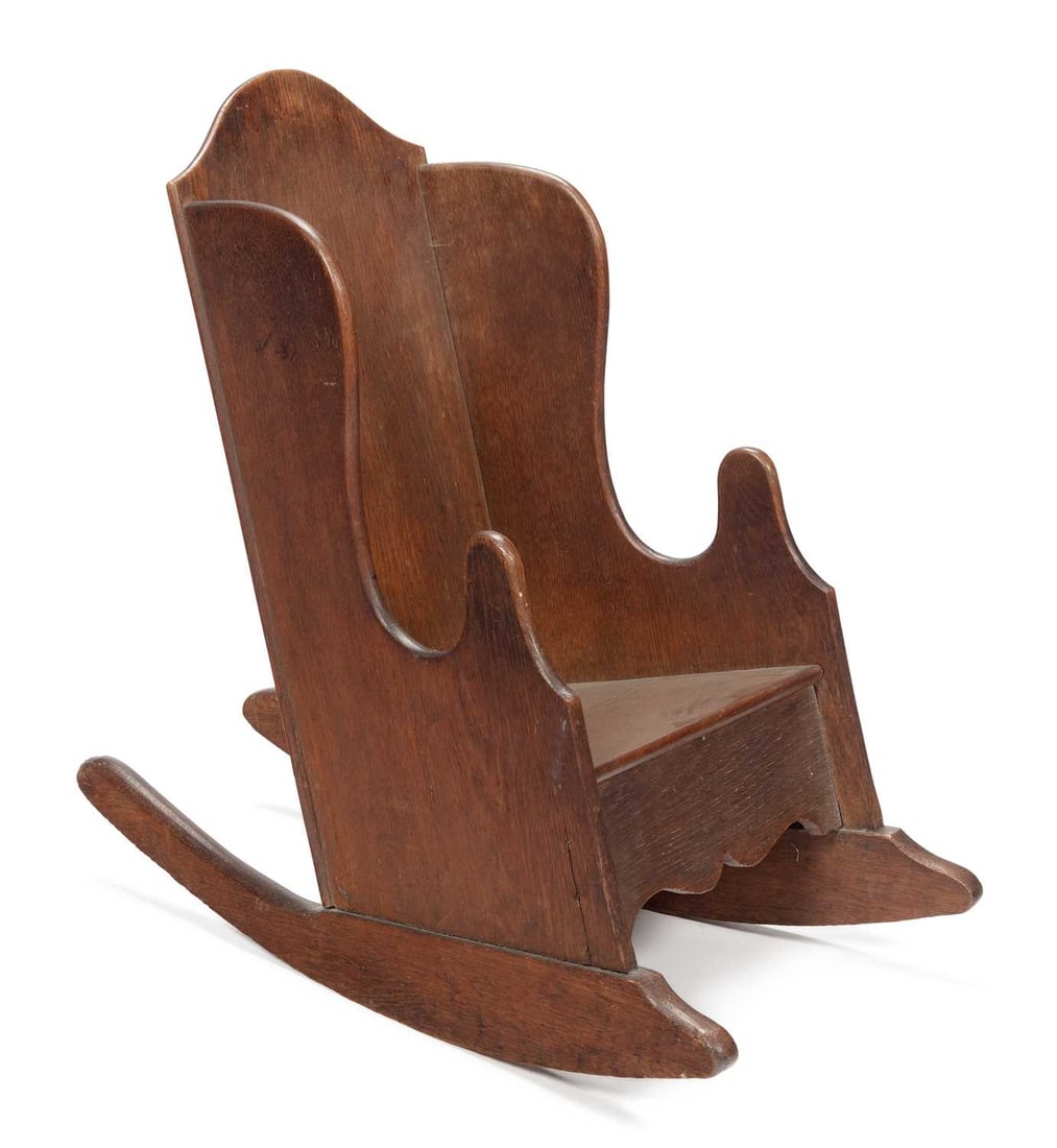 A CHILD'S OAK LAMBING CHAIR 19TH CENTURY: of boarded construction, the shaped wing back above a solid seat and a shaped apron, raised on rocker feet. Height of back 70cm