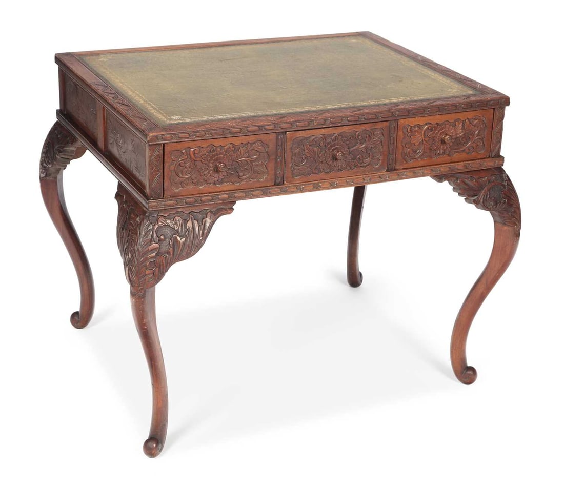 A CARVED HARDWOOD WRITING TABLE EARLY 20TH CENTURY: the rectangular top inset with a gilt tooled leather writing surface within a chip carved edge, the frieze carved in relief with panels of peony blooms among scrolling foliage, raised on cabriole legs