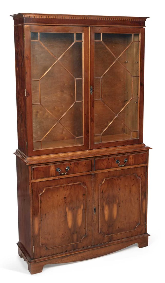 A REPRODUCTION YEW WOOD BOOKCASE: in two sections, the dentil cornice above a pair of astragal glazed doors enclosing shelves, the base with two frieze drawers above a pair of panelled cupboard doors with burr yew panels, raised on br
