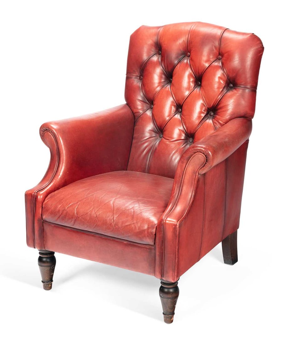 A LAURA ASHLEY BUTTON BACK LEATHER ARMCHAIR: upholstered in oxblood leather, the deep buttoned back above scrolled arms and a sprung seat, raised on turned front legs. Height of back 94cm