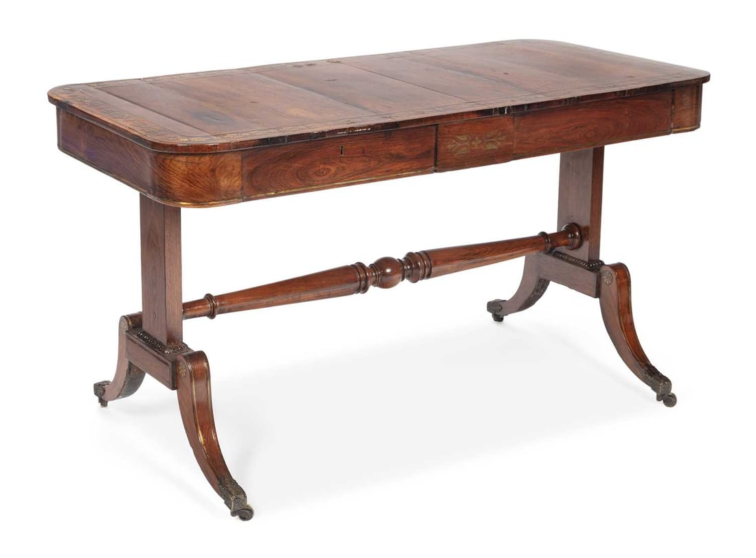 A REGENCY BRASS INLAID ROSEWOOD SOFA TABLE: the rectangular twin flap top with rounded corners, inlaid throughout with a broad band of brass foliate scrolls, anthemia and paterae within line inlay, above two frieze drawers, raised on trestle