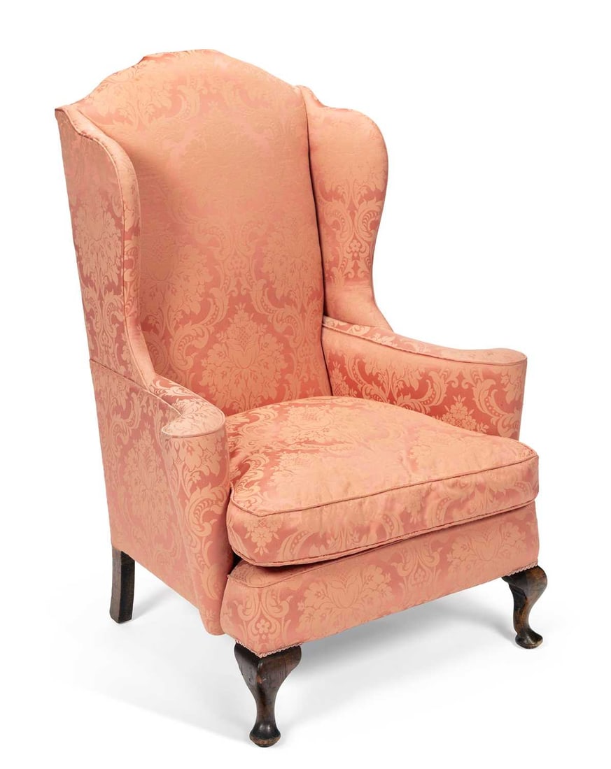 A WING-BACK ARMCHAIR: in the George I taste, upholstered in salmon damask, the arched back between outswept wings above scrolled arms and a loose cushion seat, raised on cabriole front legs terminating in pad feet. Height 