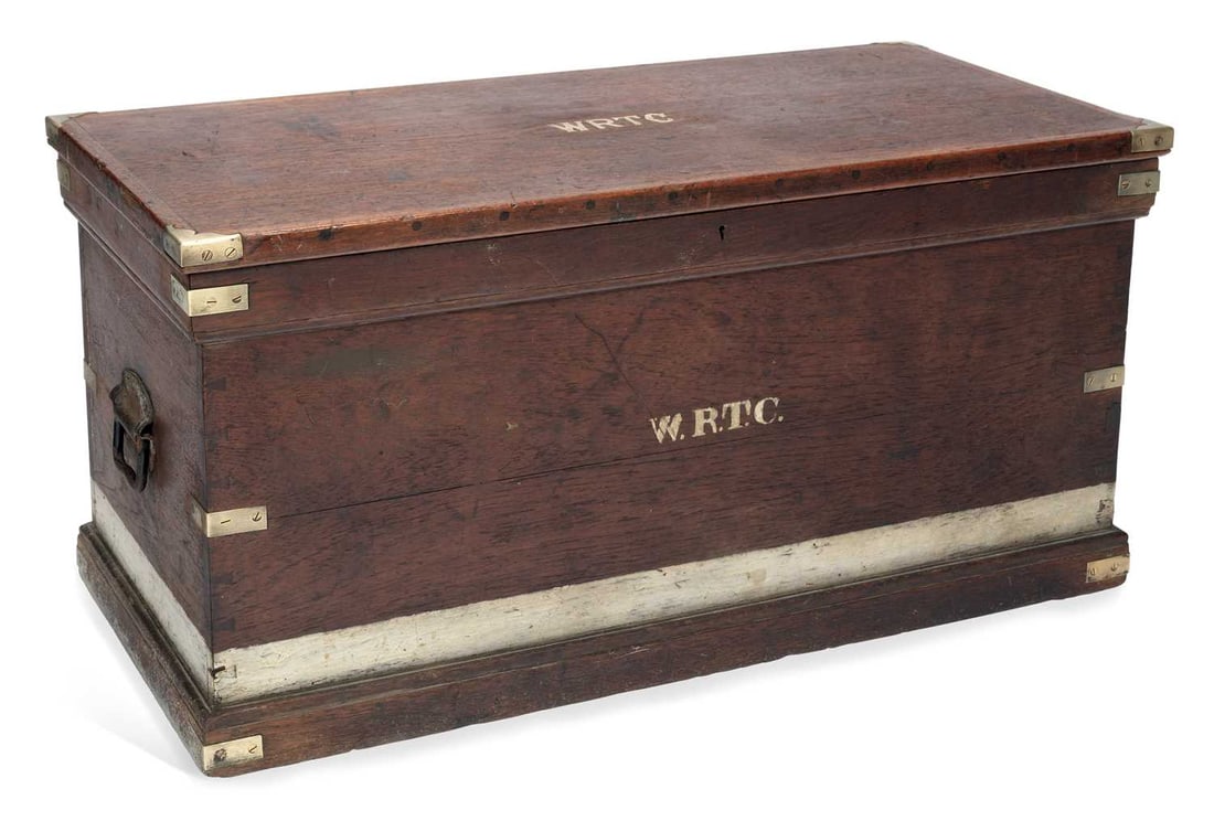 AN EARLY 20TH CENTURY BRASS-BOUND TEAK TRUNK: the hinged cover centred by brass initials WRTC, the interior with two lift-out trays. 47.5cm high, 96cm wide, 47cm deep