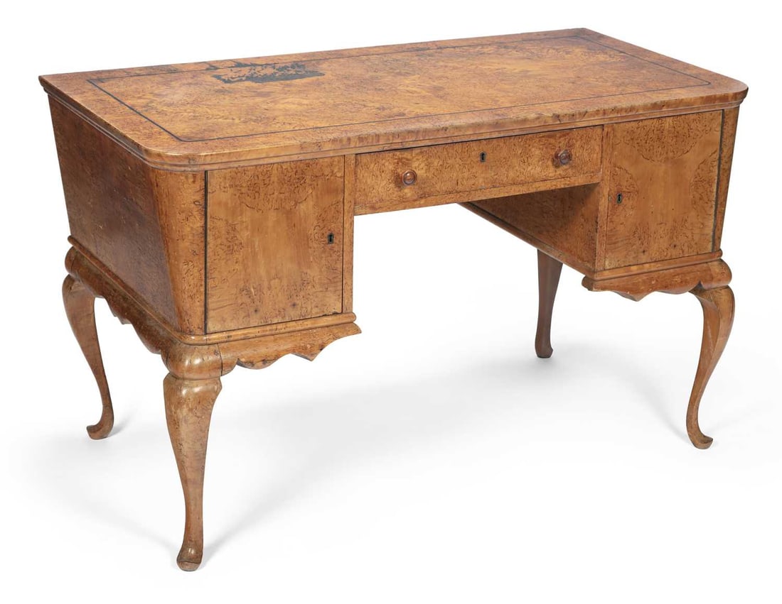 AN EARLY 20TH CENTURY CONTINENTAL BURR ELM DESK: the quarter-veneered top with ebony stringing above canted sides, the front with a drawer and a pair of cupboard doors, raised on cabriole legs terminating in pad feet. 80cm high, 130cm wide, 66cm