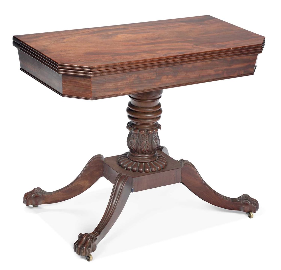 A WILLIAM IV MAHOGANY FOLDOVER TEA TABLE: the rectangular swivel top with canted corners and reeded edge, on a lobed and acanthus carved baluster column, raised on a platform base with four reeded downswept legs terminating in carved paw