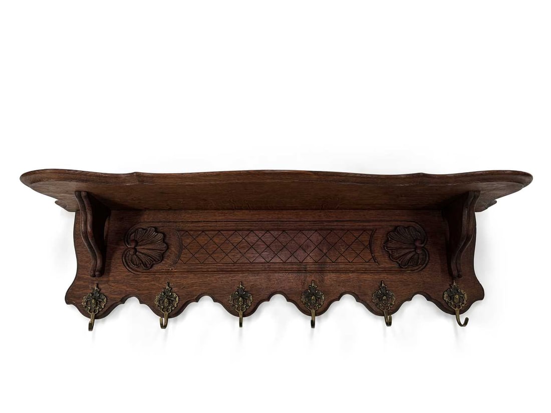 A CARVED OAK WALL SHELF AND COAT RACK: in the Louis XV taste, the shaped and moulded shelf on scroll brackets above a back panel carved with shells flanking a lattice panel, the shaped lower edge fitted with six pierced brass hooks. 91cm