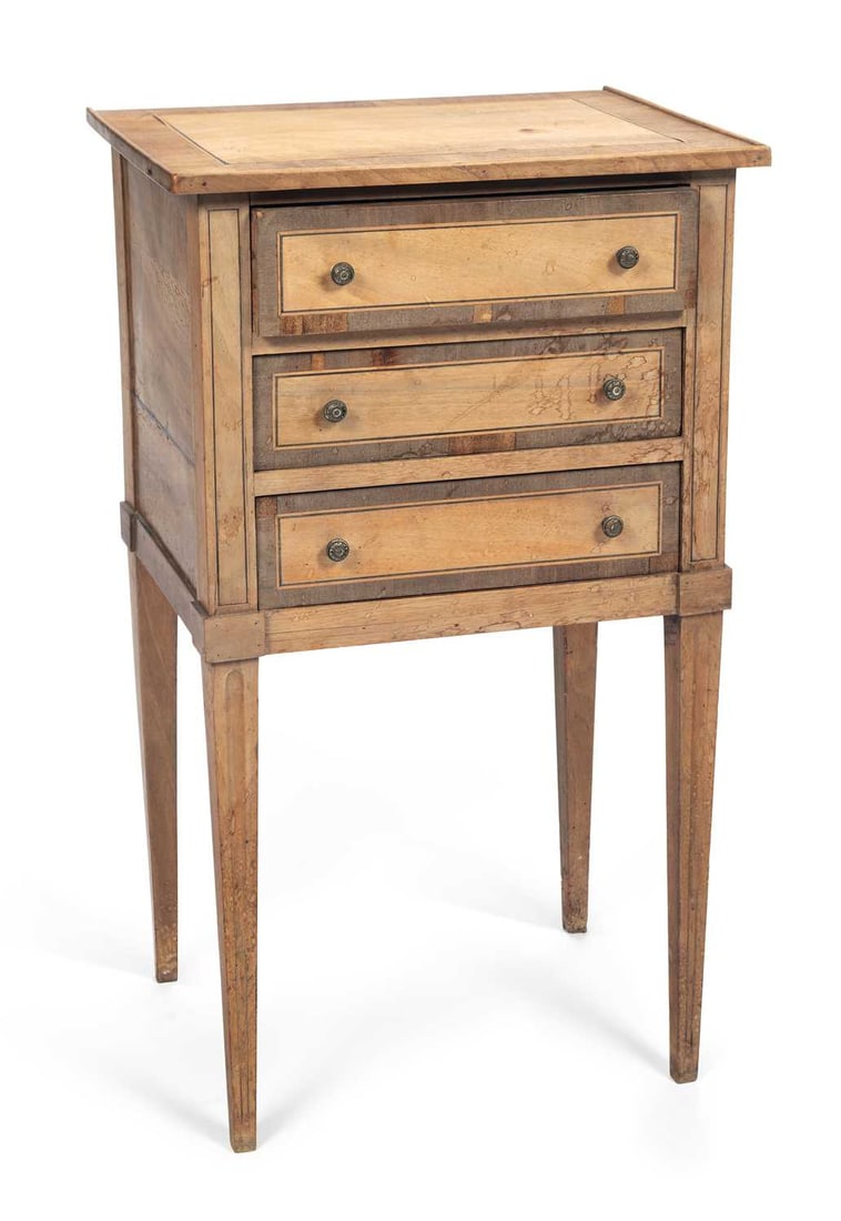 A CONTINENTAL FRUITWOOD NIGHT TABLE: in the Louis XVI taste, the rectangular top within a crossbanded and line inlaid border, above three long drawers with brass knob handles, the canted stiles with line inlay, raised on square tapering 